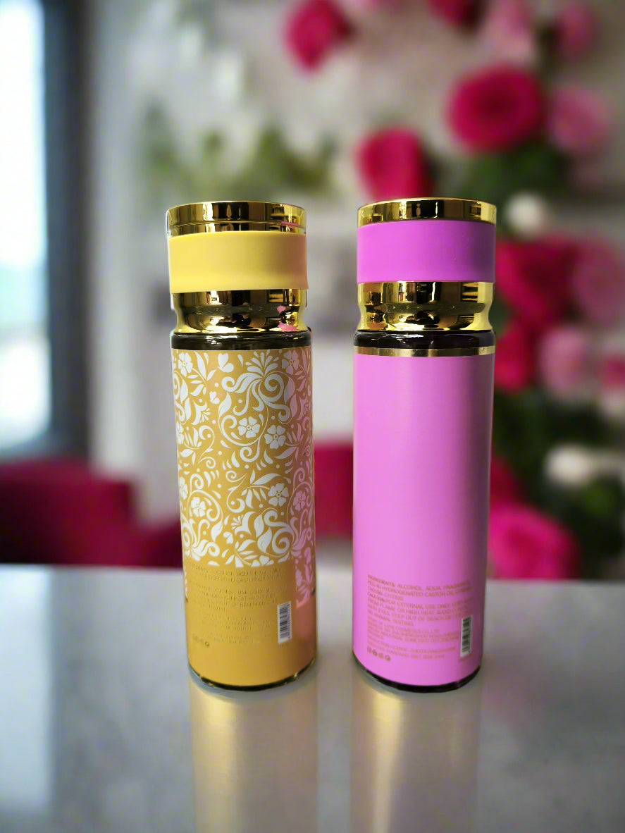 Two insulated travel mugs, one yellow with floral design and gold lid, the other pink with gold lid, on a textured surface.
