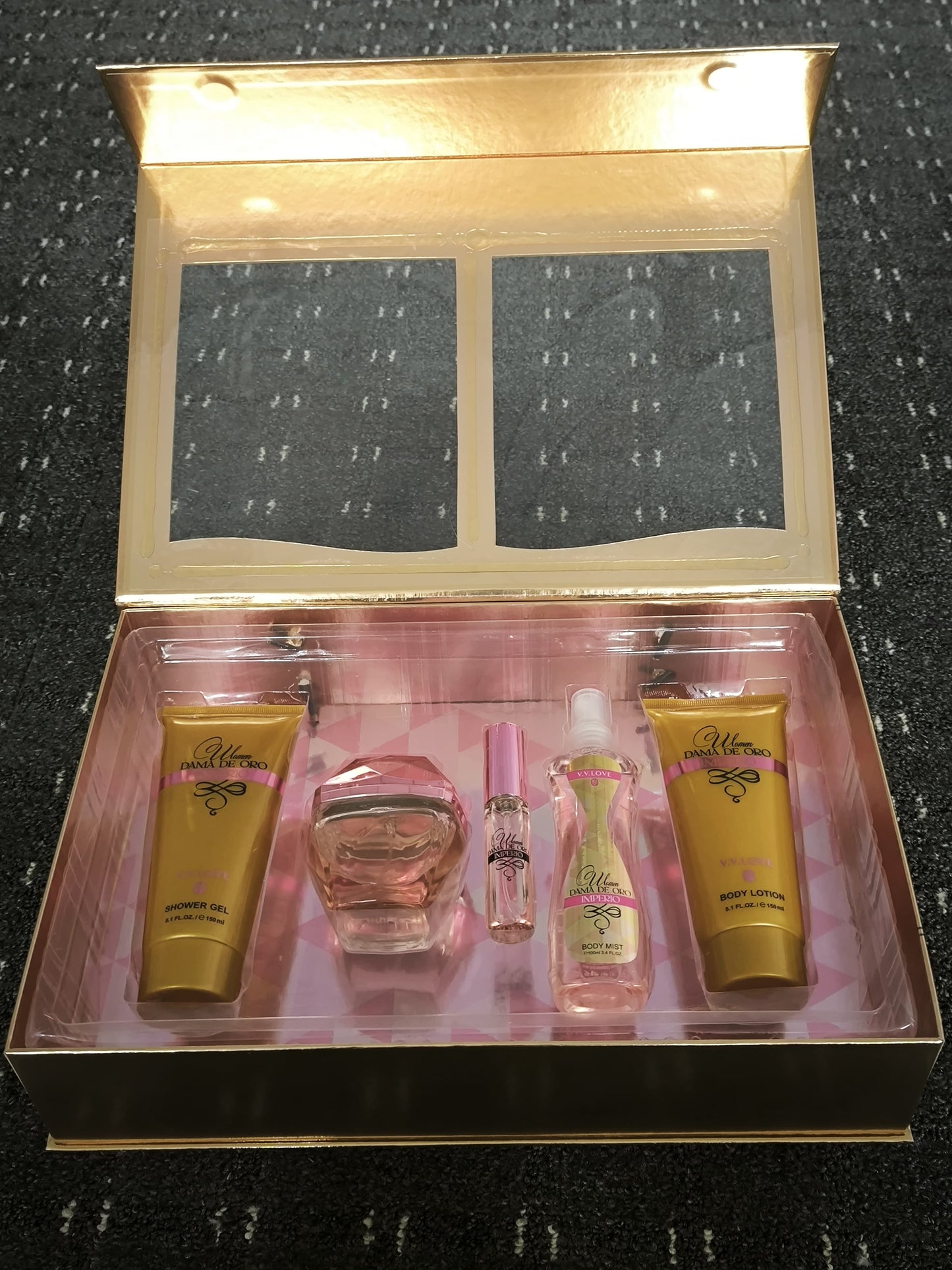 Cosmetic set with products including a bottle and two gold containers in an open box on a textured surface.