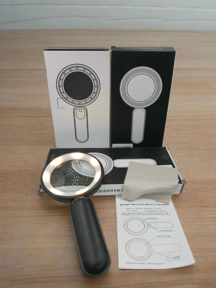 Handheld magnifying glass with packaging, cloth, and user manual on a white surface.