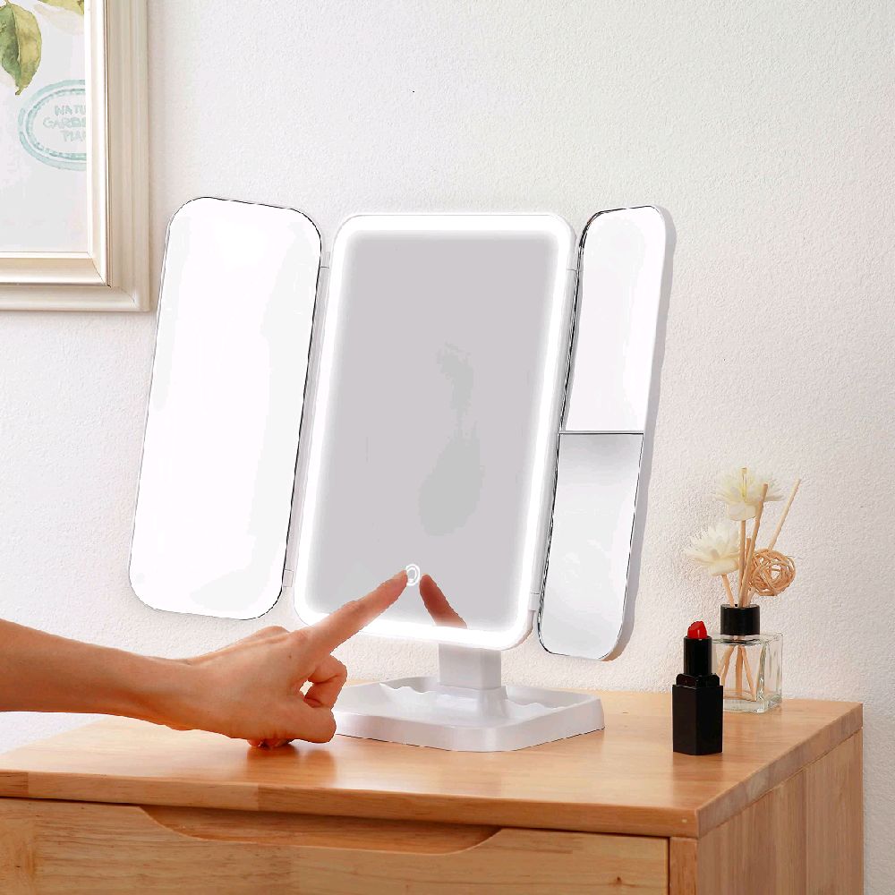 Person using a light-up vanity mirror on a wooden dresser.